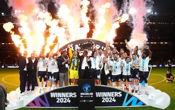 England players and coaches celebrate with the trophy following victory in Soccer Aid for UNICEF 2024 at Stamford Bridge